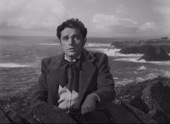 Movie still from “My Cousin Rachel” (1952), directed by Henry Koster – A black and white photo of a man sitting on a rock near the ocean; Medium shot, Low angle