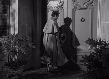 Movie still from “My Cousin Rachel” (1952), directed by Henry Koster – A man wearing a cape walking in front of a door; Wide shot, High angle