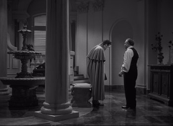Movie still from “My Cousin Rachel” (1952), directed by Henry Koster – Two men standing next to each other near a pillar; Medium shot, High angle