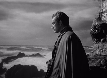 Movie still from “My Cousin Rachel” (1952), directed by Henry Koster – A black and white photo of a man standing in front of the ocean; Medium shot, Low angle