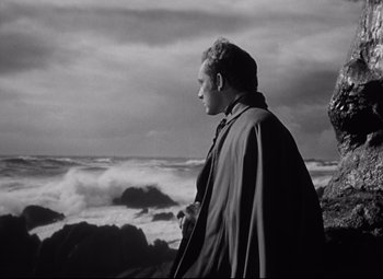Movie still from “My Cousin Rachel” (1952), directed by Henry Koster – A black and white photo of a man standing in front of the ocean; Medium shot, Low angle