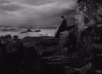 Movie still from “My Cousin Rachel” (1952), directed by Henry Koster – A person sitting on a rock near the ocean; Extreme Wide shot, Low angle