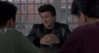 Movie still from “My Cousin Vinny” (1992), directed by Jonathan Lynn – A man sitting at a table with his hands clasped together; Medium shot, Over the shoulder angle