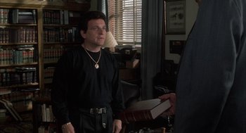 Movie still from “My Cousin Vinny” (1992), directed by Jonathan Lynn – A man standing in front of a book in a living room; Medium shot, Over the shoulder angle