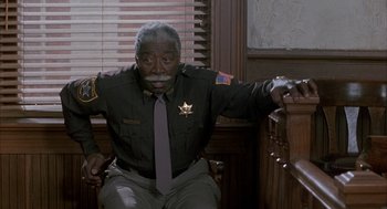 Movie still from “My Cousin Vinny” (1992), directed by Jonathan Lynn – A police officer sitting in a chair in front of a window; Medium shot, High angle