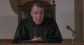 Movie still from “My Cousin Vinny” (1992), directed by Jonathan Lynn – A man sitting in a chair in a court room; Close Up shot, Low angle
