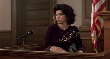 Movie still from “My Cousin Vinny” (1992), directed by Jonathan Lynn – A woman sitting at a table in front of a microphone; Medium shot, High angle