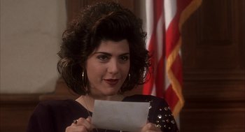 Movie still from “My Cousin Vinny” (1992), directed by Jonathan Lynn – A woman holding a piece of paper in front of an american flag; Close Up shot, High angle