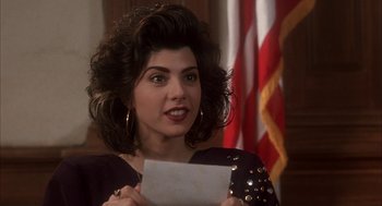 Movie still from “My Cousin Vinny” (1992), directed by Jonathan Lynn – A woman holding a piece of paper in front of an american flag; Close Up shot, High angle