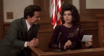 Movie still from “My Cousin Vinny” (1992), directed by Jonathan Lynn – A man and a woman sitting in front of microphones in a courtroom; Medium shot, High angle