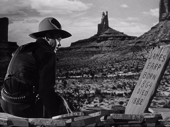 Movie still from “My Darling Clementine” (1946), directed by John Ford – An old photo of a man sitting on a bench in the desert; Medium shot, Low angle