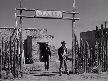 Movie still from “My Darling Clementine” (1946), directed by John Ford – A man and a woman standing under a jail sign; Wide shot, Low angle