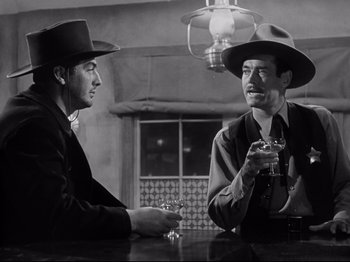 Movie still from “My Darling Clementine” (1946), directed by John Ford – Two men are sitting at a table with a drink; Medium shot, Over the shoulder angle