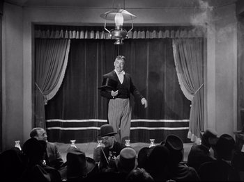 Movie still from “My Darling Clementine” (1946), directed by John Ford – An old man is on a stage in front of an audience; Wide shot, Low angle