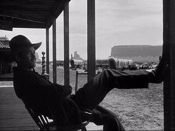 Movie still from “My Darling Clementine” (1946), directed by John Ford – A black and white photo of a man sitting in a rocking chair; Wide shot, Low angle