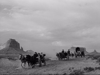 Movie still from “My Darling Clementine” (1946), directed by John Ford – A black and white photo of people riding in a covered wagon; Wide shot, Low angle