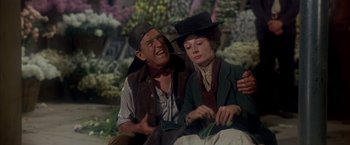 Movie still from “My Fair Lady” (1964), directed by George Cukor – A man and a woman sitting next to each other on the ground; Medium shot, Over the shoulder angle