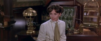 Movie still from “My Fair Lady” (1964), directed by George Cukor – A woman sitting in front of a desk wearing a suit and tie; Close Up shot, Over the shoulder angle
