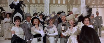 Movie still from “My Fair Lady” (1964), directed by George Cukor – A group of people wearing fancy hats in a room; Medium shot, Low angle