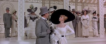 Movie still from “My Fair Lady” (1964), directed by George Cukor – A man and a woman wearing hats and a dress; Medium shot, Low angle