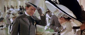 Movie still from “My Fair Lady” (1964), directed by George Cukor – A man in a suit and a top hat adjusts his hat; Close Up shot, Over the shoulder angle