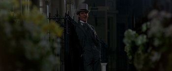 Movie still from “My Fair Lady” (1964), directed by George Cukor – A man in a top hat and suit standing next to a fence; Medium shot, Low angle
