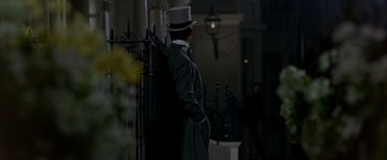Movie still from “My Fair Lady” (1964), directed by George Cukor – A man in a top hat and a long black coat standing in front of a fence; Wide shot, Over the shoulder angle