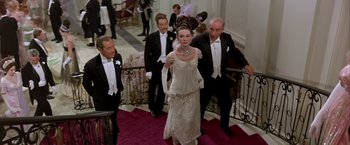 Movie still from “My Fair Lady” (1964), directed by George Cukor – A group of people in formal wear walking down a red carpet; Medium shot, Low angle