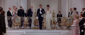 Movie still from “My Fair Lady” (1964), directed by George Cukor – A man and a woman in formal wear standing in front of a crowd; Wide shot, Low angle