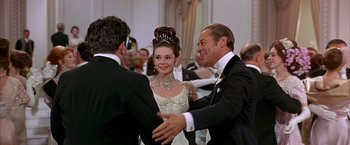 Movie still from “My Fair Lady” (1964), directed by George Cukor – Two men and a woman in formal wear shaking hands; Medium shot, Over the shoulder angle