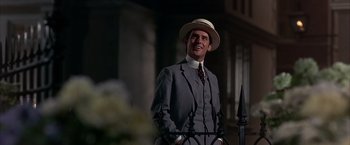 Movie still from “My Fair Lady” (1964), directed by George Cukor – A man in a suit and hat standing next to a fence; Medium shot, Low angle