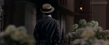 Movie still from “My Fair Lady” (1964), directed by George Cukor – A man wearing a suit and a straw hat is looking over a fence; Medium shot, Over the shoulder angle
