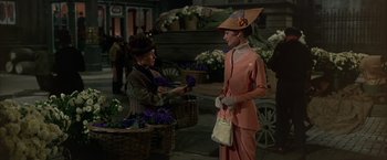 Movie still from “My Fair Lady” (1964), directed by George Cukor – A woman in an orange dress and a woman in an orange hat; Medium shot, Over the shoulder angle