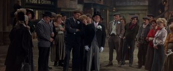 Movie still from “My Fair Lady” (1964), directed by George Cukor – A group of people standing around each other wearing suits and hats; Wide shot, High angle