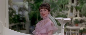 Movie still from “My Fair Lady” (1964), directed by George Cukor – A woman in a pink dress sitting at a table; Close Up shot, Over the shoulder angle