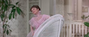 Movie still from “My Fair Lady” (1964), directed by George Cukor – A woman in a pink dress standing in front of a white chair; Medium shot, Low angle
