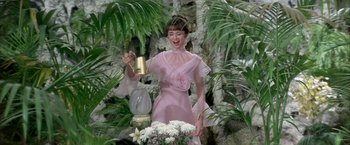Movie still from “My Fair Lady” (1964), directed by George Cukor – A woman in a pink dress holding a champagne bottle; Medium shot, Low angle