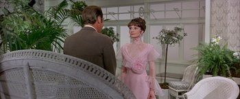 Movie still from “My Fair Lady” (1964), directed by George Cukor – A man and a woman in a pink dress in front of a chair; Medium shot, Over the shoulder angle