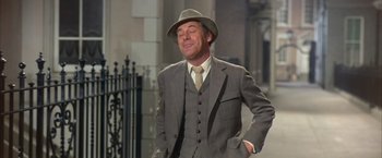 Movie still from “My Fair Lady” (1964), directed by George Cukor – A man in a suit and hat standing in front of a building; Medium shot, Low angle