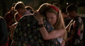 Movie still from “My Father the Hero” (1994), directed by Steve Miner – A girl is hugging another girl in a crowd of people; Medium shot, Over the shoulder angle