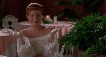 Movie still from “My Father the Hero” (1994), directed by Steve Miner – A woman in a white blouse is sitting at a table; Medium shot, Low angle