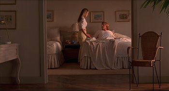 Movie still from “My Father the Hero” (1994), directed by Steve Miner – A woman standing next to a man on a bed; Wide shot, High angle