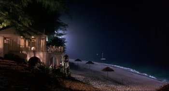 Movie still from “My Father the Hero” (1994), directed by Steve Miner – A night time view of a beach with umbrellas and a boat in the background; Extreme Wide shot, High angle