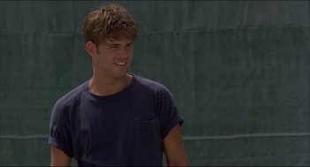 Movie still from “My Father the Hero” (1994), directed by Steve Miner – A young man smiles while holding a racquet; Close Up shot, Over the shoulder angle