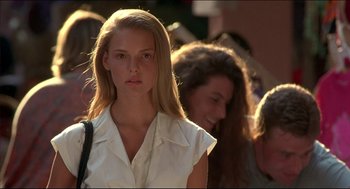 Movie still from “My Father the Hero” (1994), directed by Steve Miner – A woman with long blonde hair is standing in a crowd of people; Close Up shot, Over the shoulder angle