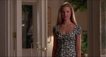 Movie still from “My Father the Hero” (1994), directed by Steve Miner – A woman in a floral dress standing next to a door; Medium shot, Over the shoulder angle