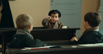 Movie still from “My Father's Glory” (1990), directed by Yves Robert – Two boys are sitting at a desk and one is pointing at the camera; Medium shot, Over the shoulder angle