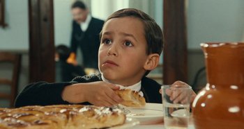 Movie still from “My Father's Glory” (1990), directed by Yves Robert – A young boy sitting at a table eating a piece of bread; Close Up shot, Over the shoulder angle