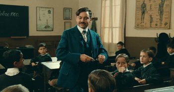 A man in a blue suit is standing in front of a group of children