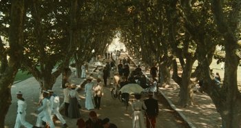 Movie still from “My Father's Glory” (1990), directed by Yves Robert – A group of people walking down a tree lined street; Extreme Wide shot, High angle